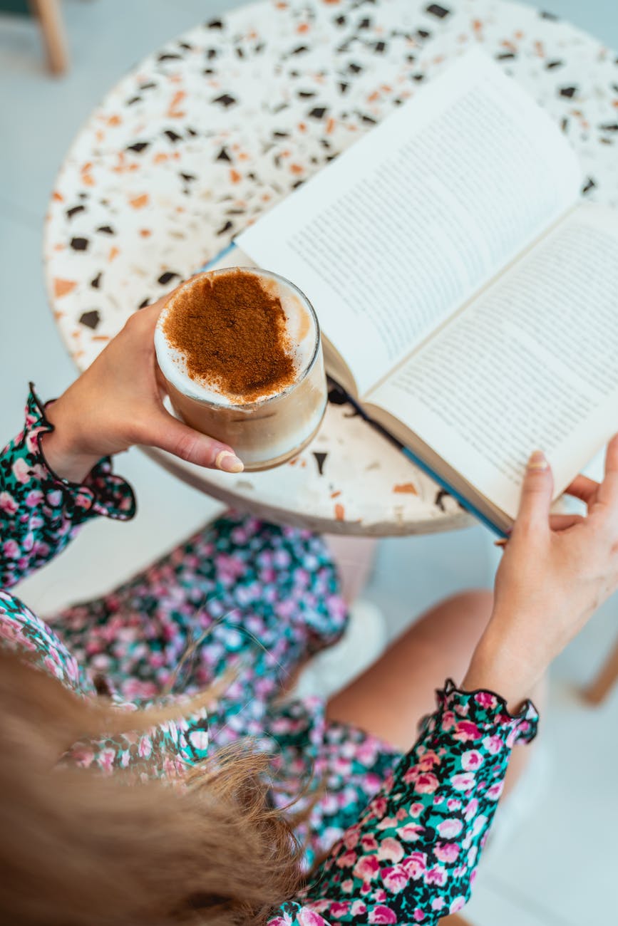 photo of woman reading book while holding iced latte